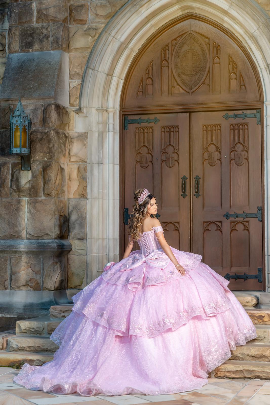 Jayden con vestido rosa de XV años y tiara, de pie frente a la puerta de una iglesia de piedra